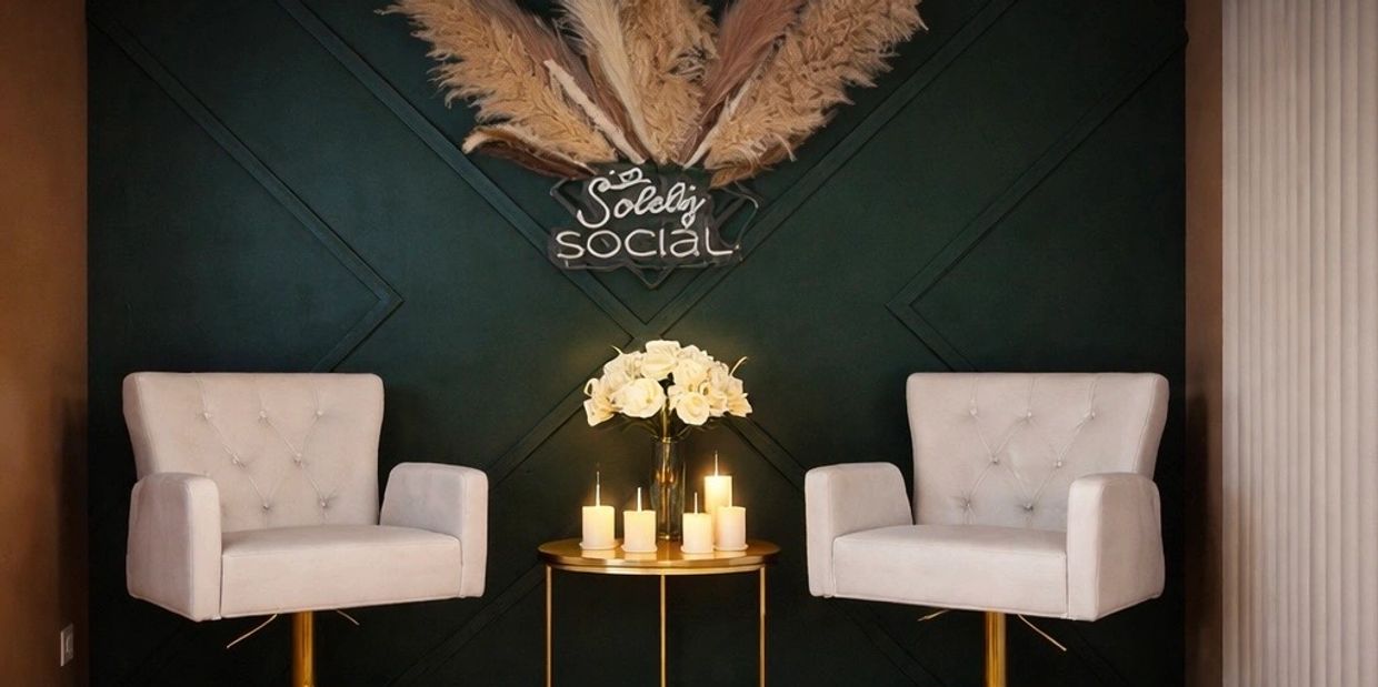 Elegant seating area with two white chairs and a candlelit table against a dark green wall.