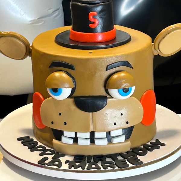 A detailed cake shaped like a cartoon bear wearing a hat with a red number 5.