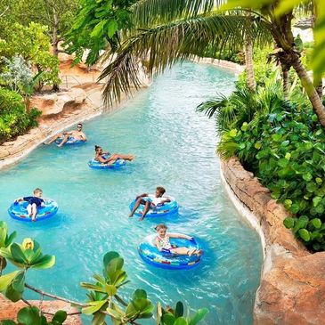 People floating on a lazy river surrounded by tropical plants.