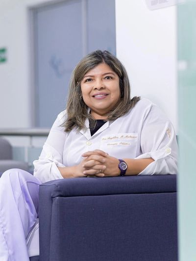 Smiling female medical professional in white coat sitting on a chair indoors.