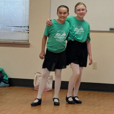 Two girls in green T-shirts and black skirts posing together indoors.