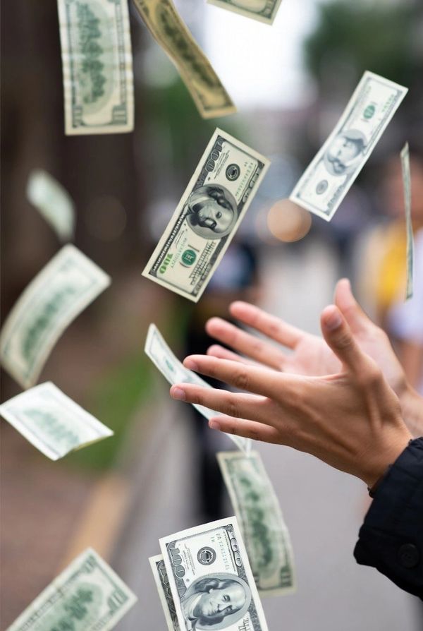 Hands reaching out as dollar bills float in the air outdoors.
