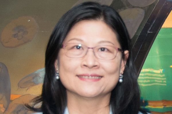 Smiling woman with glasses and pearl earrings indoors.