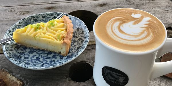 A slice of lemon tart and a cup of latte with swan latte art.