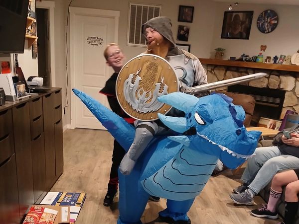 Person in blue dragon costume holding shield and sword indoors.