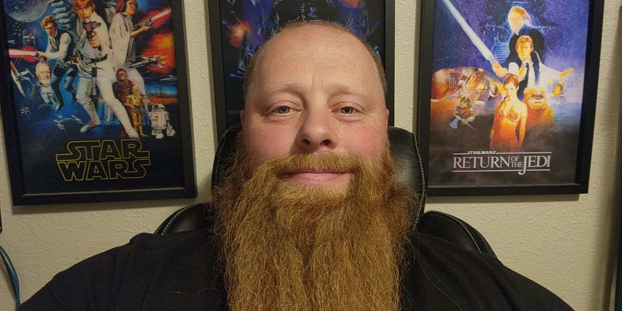 Man with a long beard in front of Star Wars posters.
