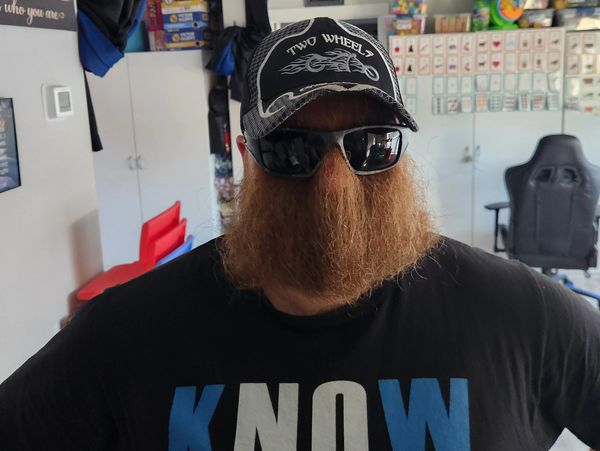 Man with big beard, sunglasses, and cap indoors.