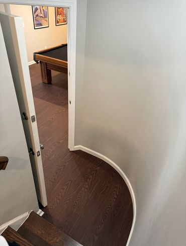 Curved wooden floor with open door leading to a room with a pool table.