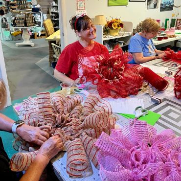 Women crafting festive wreaths with vibrant ribbons.