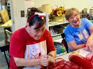Two women crafting with red mesh and smiling.
