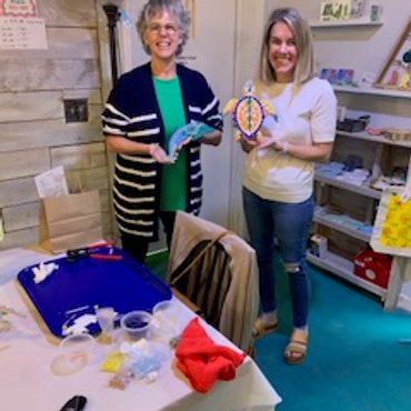 Two women holding crafts in a cozy room.