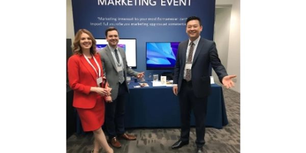 Three professionals at a marketing event booth presenting digital displays.
