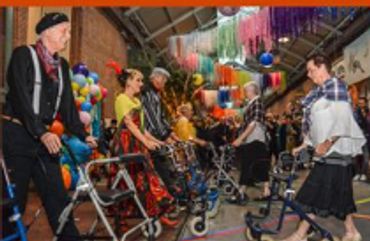 People in colorful costumes using walkers in a festive indoor setting.