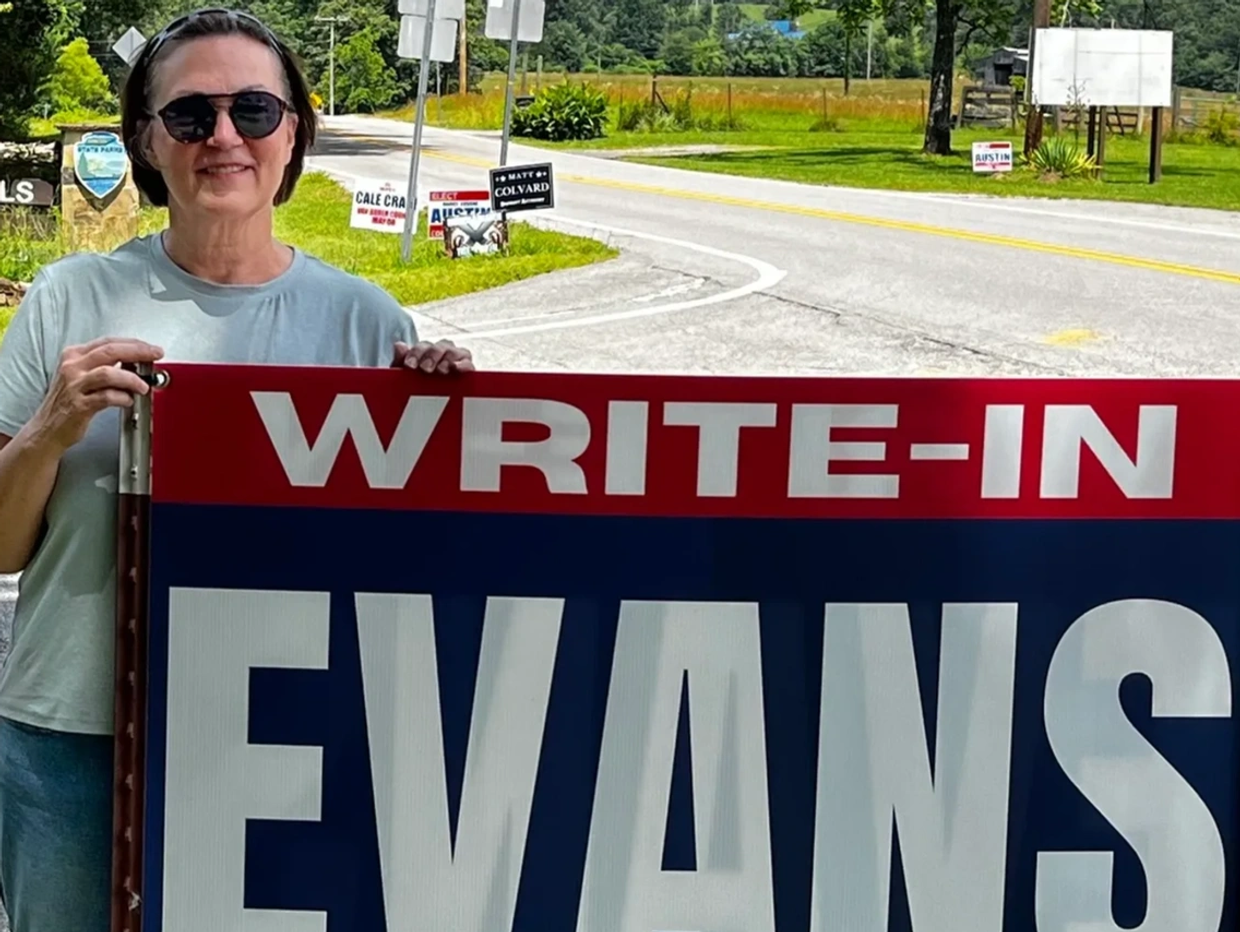A woman holding a large political campaign sign.