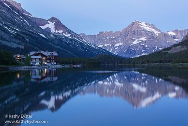 Mountain lake with cabins reflecting in calm water at dusk.