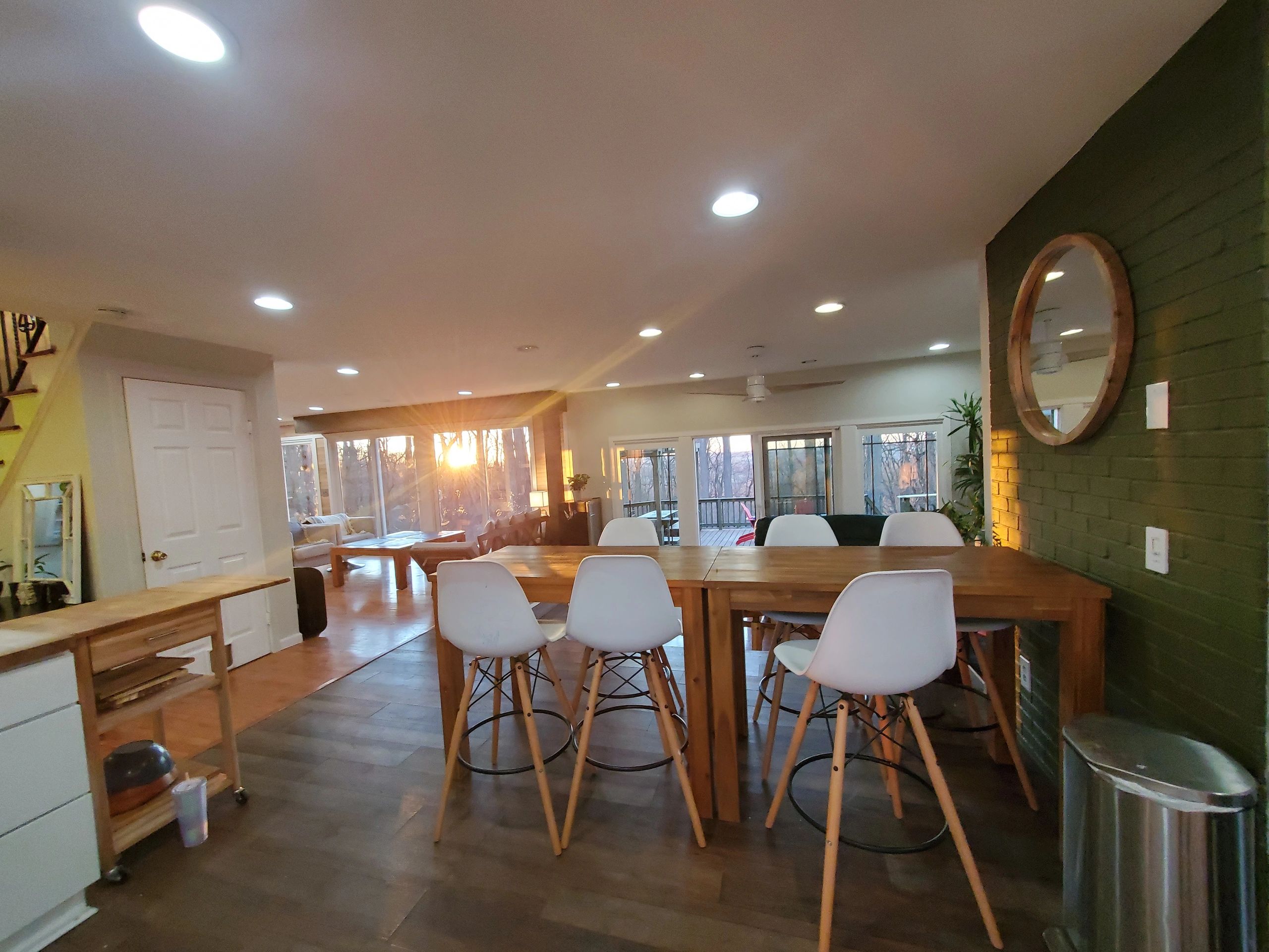 Cozy dining area with white chairs and sunset through large windows.