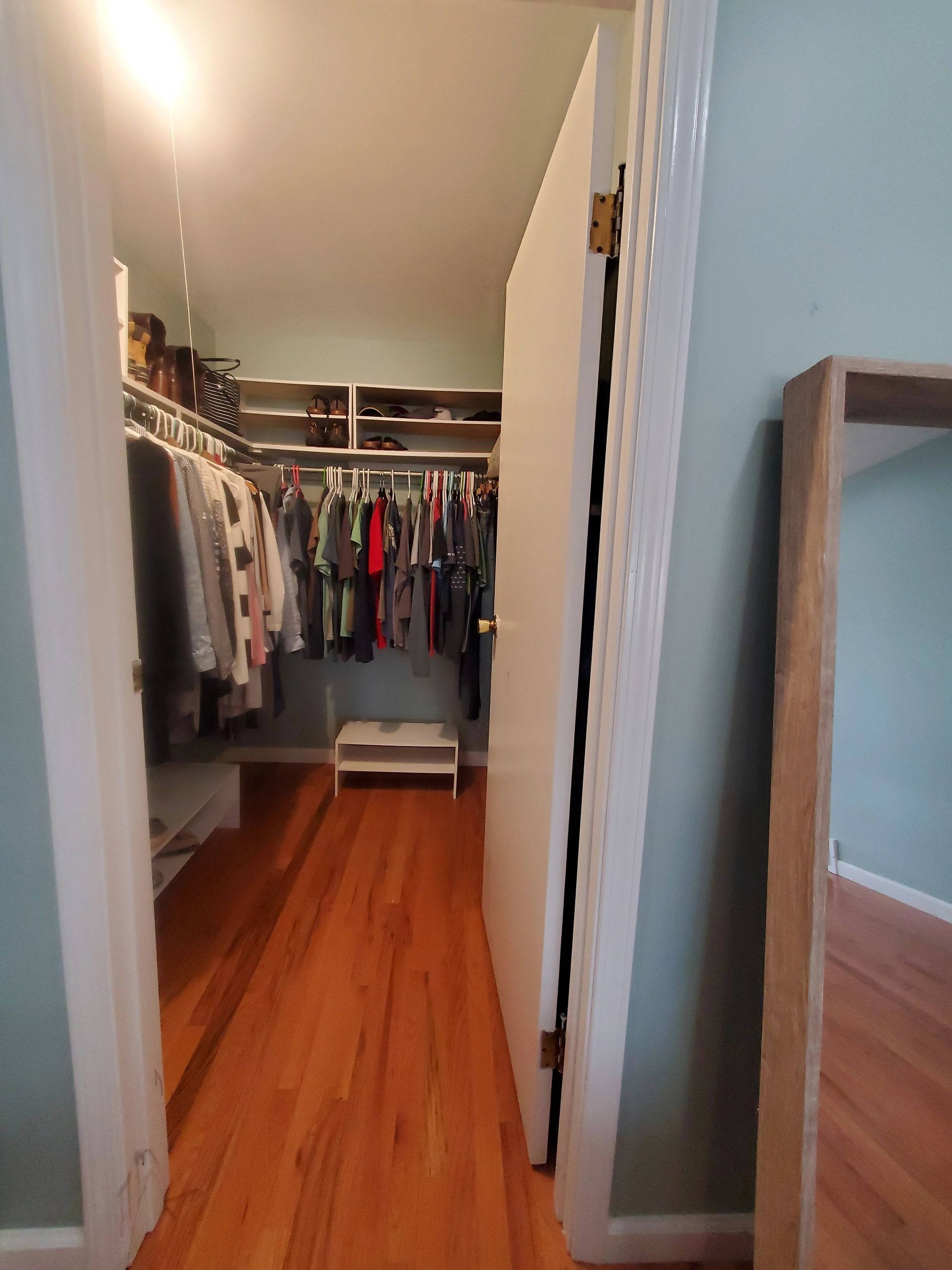 Walk-in closet with hanging clothes and wooden floor.