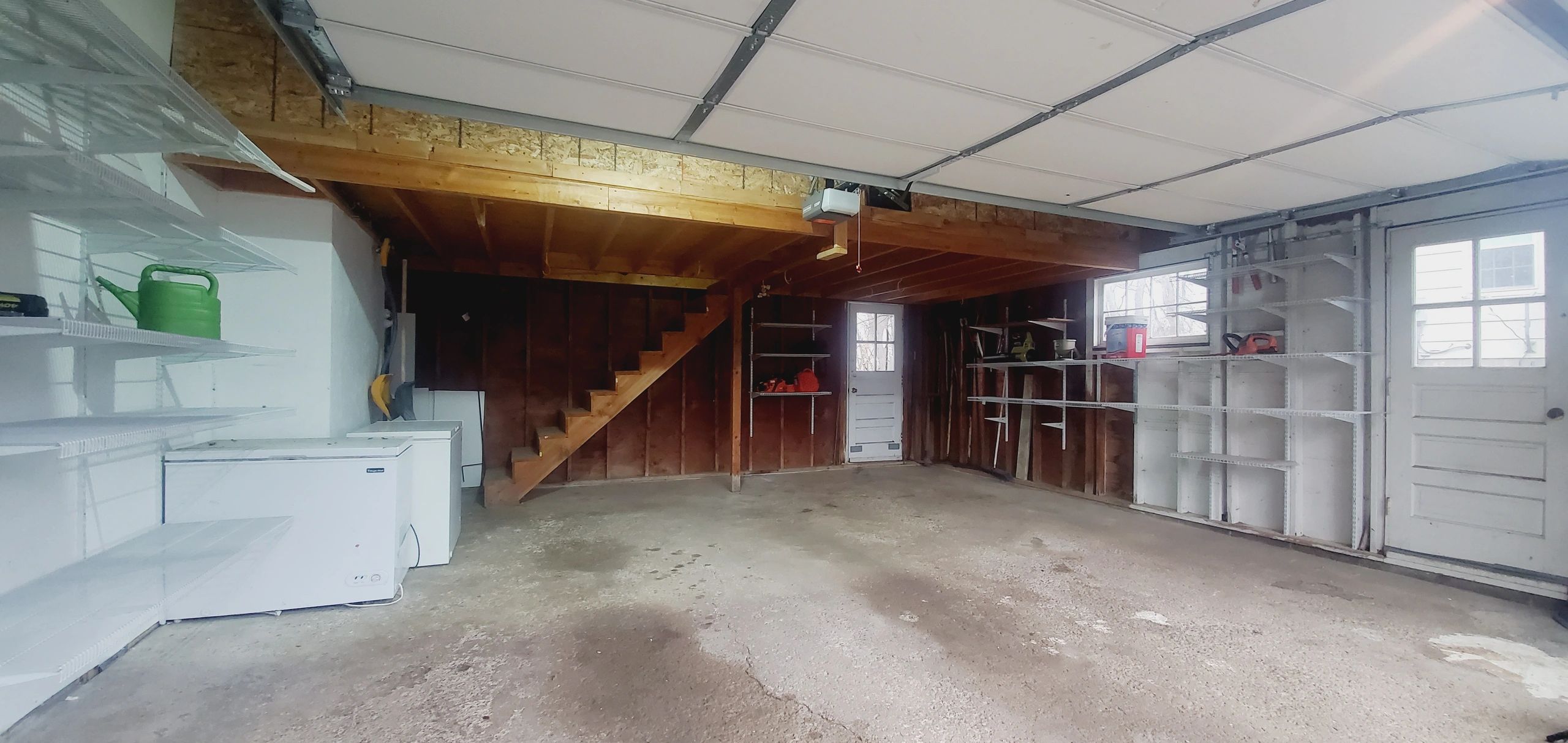Empty garage with shelving, stairs, and storage appliances.