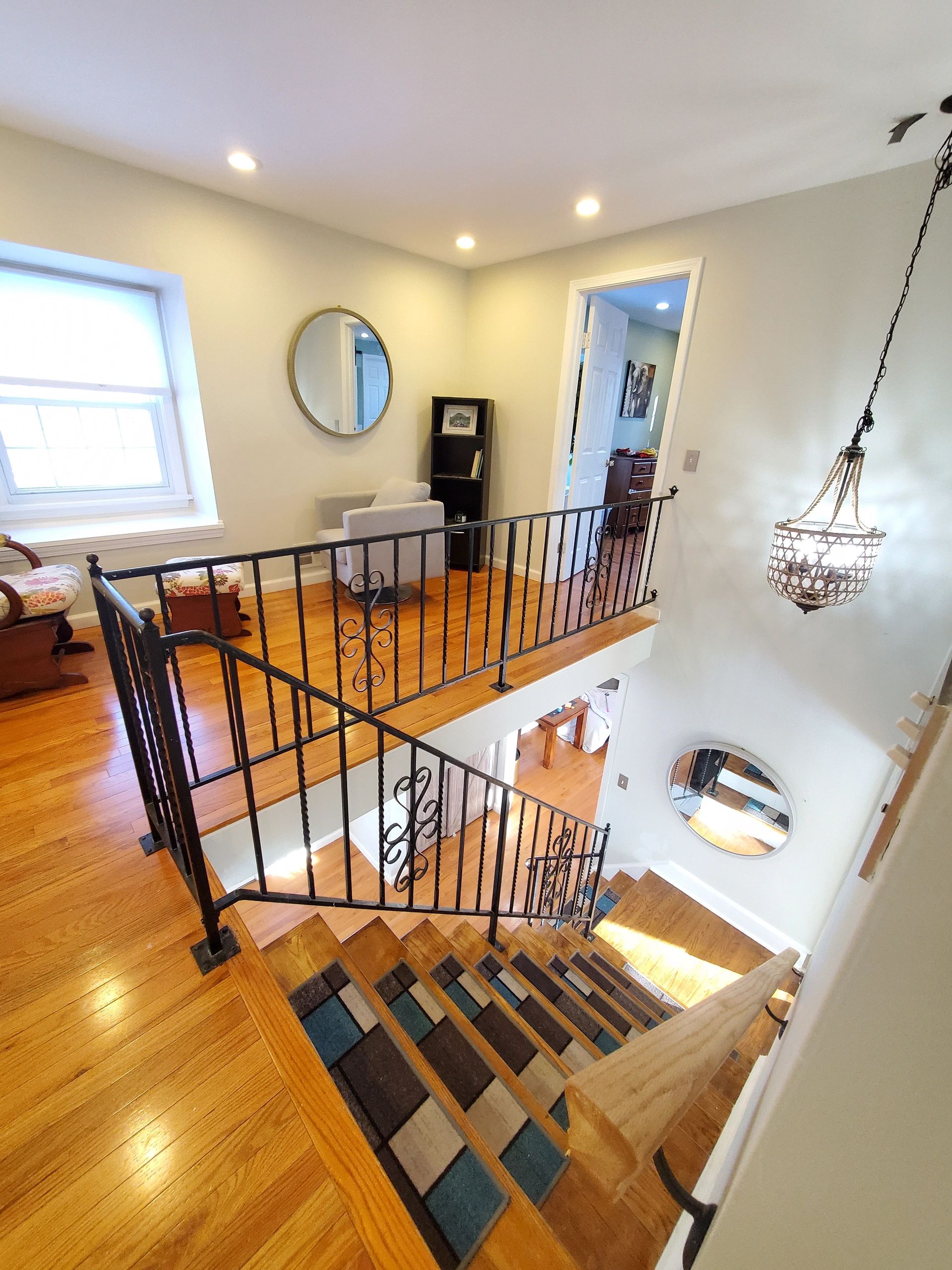 Bright stairway with wooden floors, iron railings, and round mirrors reflecting light.