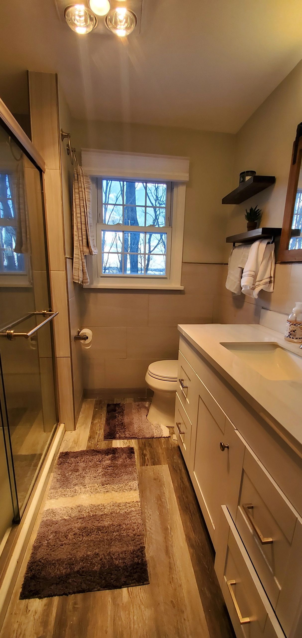 Cozy bathroom with wood flooring, white vanity, and a window showing tree branches outside.