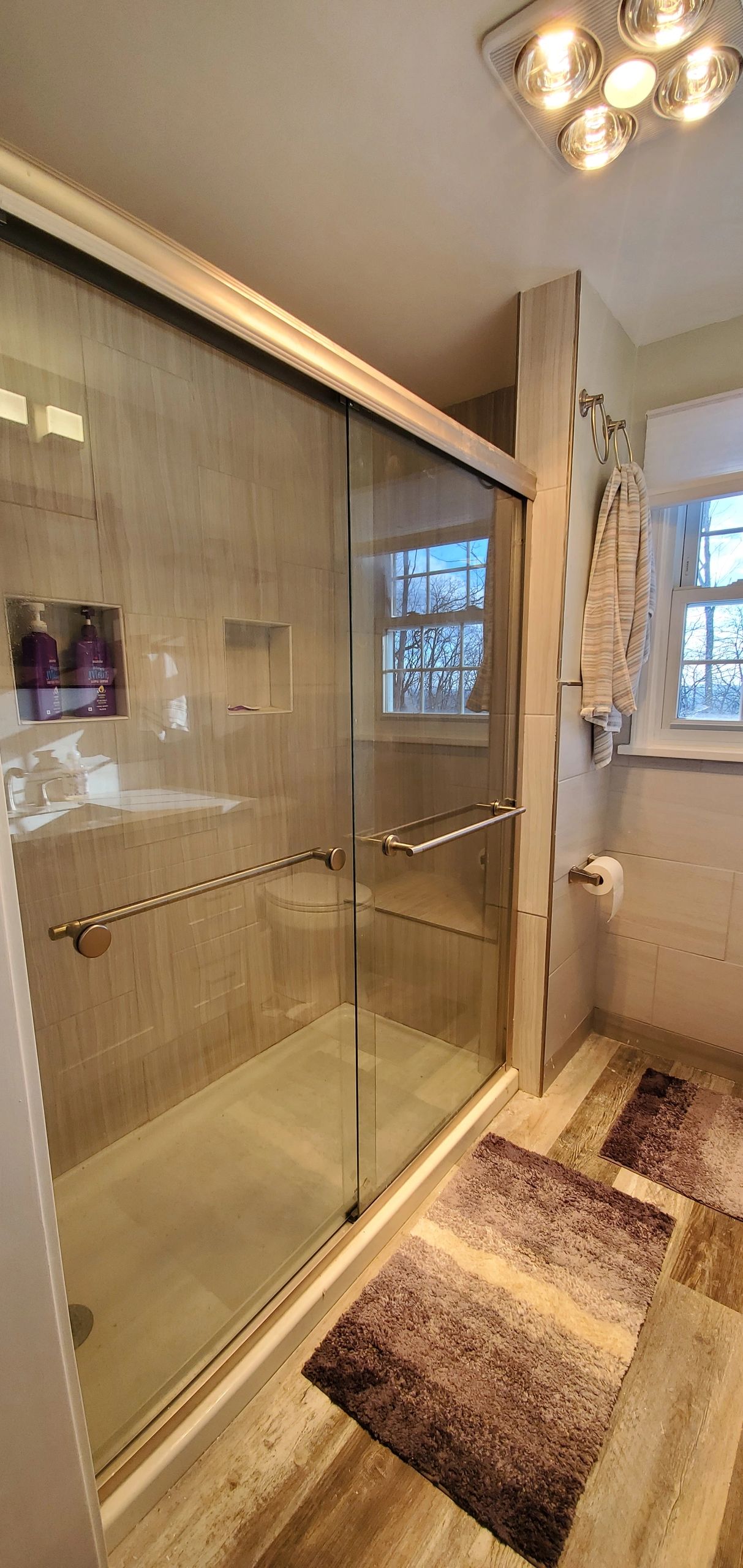 Modern bathroom with glass shower, beige tiles, and cozy rugs.