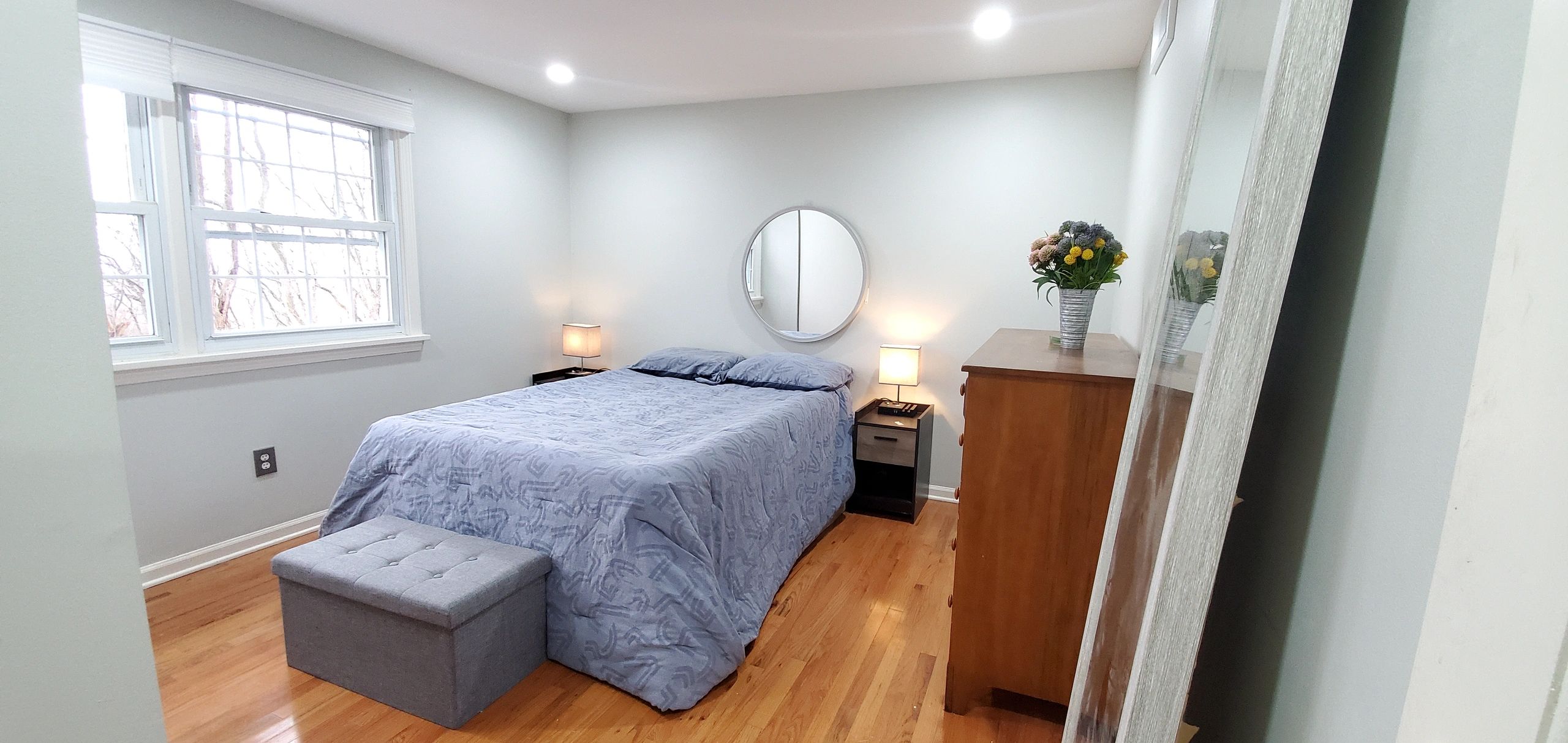 Cozy bedroom with wooden floor, blue bedding, and warm lighting.