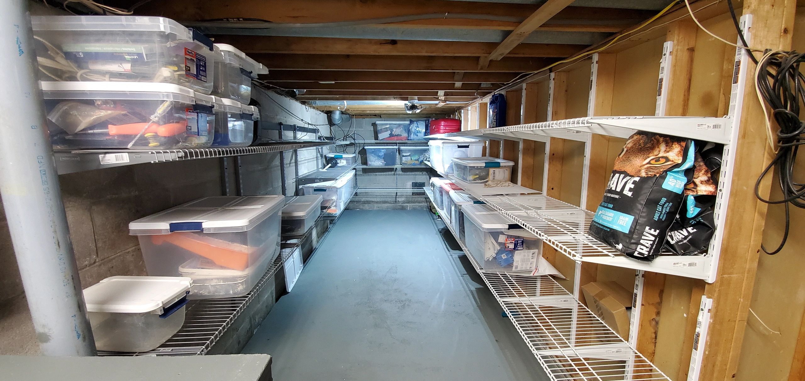 Organized basement storage with plastic bins and pet food bags on wire shelves.