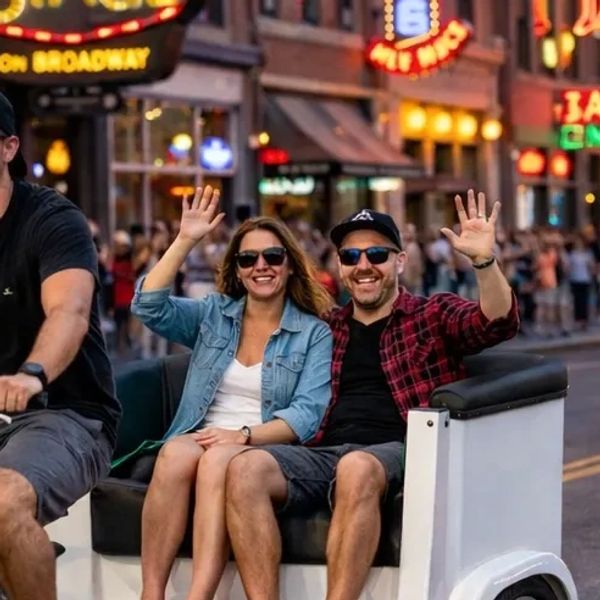 A smiling couple waves while riding a pedicab in a bustling street.