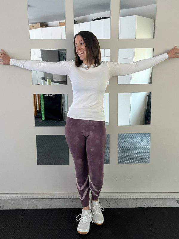 Woman in athletic wear stretching arms wide against mirrored wall.