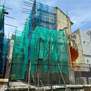 Building under renovation covered with green and blue netting against a clear sky.