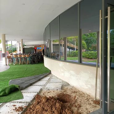 Hole dug outside a building near a bike rack with artificial grass partially rolled back.