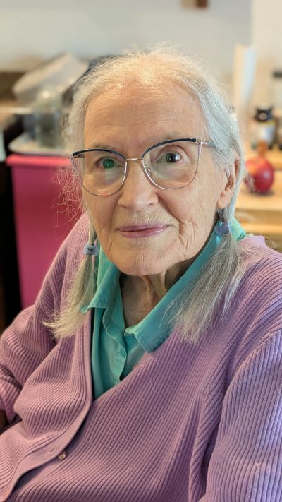 Elderly woman with glasses and braided hair smiling gently.