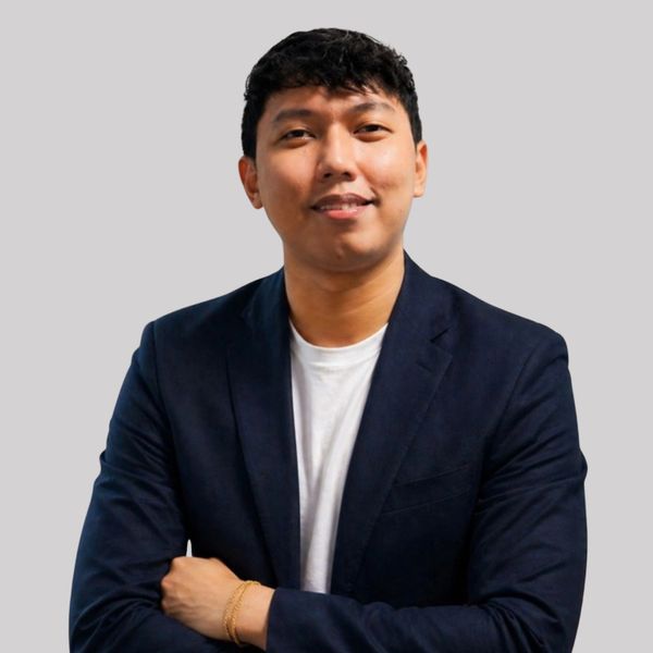 Confident young man in a navy blazer and white shirt, smiling with arms crossed.
