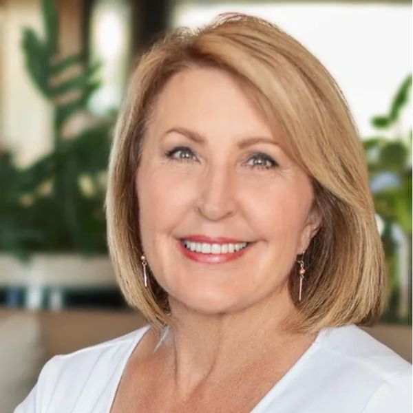 Smiling middle-aged woman with short blonde hair in a white top.