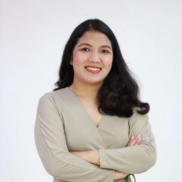 Confident woman with long dark hair smiling, arms crossed, wearing a beige top.