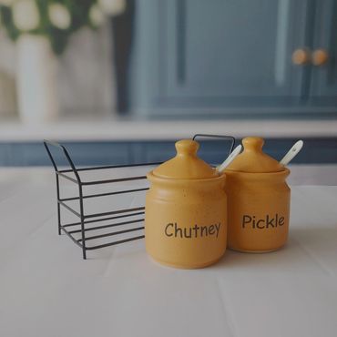 Two yellow condiment jars labeled chutney and pickle on a white surface.