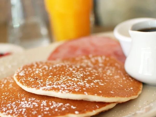 Stack of house mixed pancakes with powdered sugar and breakfast sides.