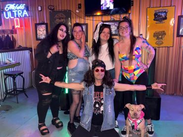 Group of friends posing joyfully in a colorful bar setting with a dog.