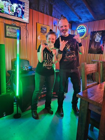 Two people posing happily with money and hand signs in a colorful bar setting.