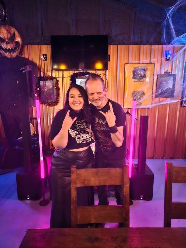 Two people smiling and making rock hand signs in a Halloween-themed room.