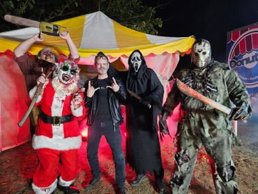 Group of people in horror-themed costumes posing at night in front of a tent.