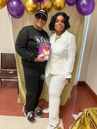Two women smiling, one holding a book against a colorful balloon background.