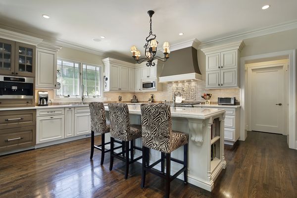 White kitchen with dark hardwood floors, zebra style chairs and dark brown hood vent.
