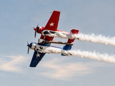 Two stunt planes flying close with smoke trails.