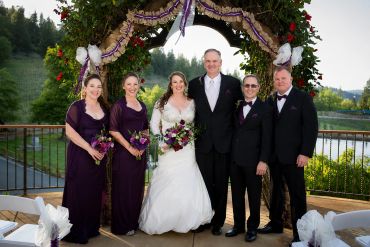 Wedding party posing under floral arch outdoors.