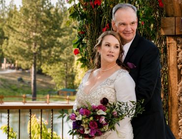Couple posing in wedding attire outdoors with bouquet.