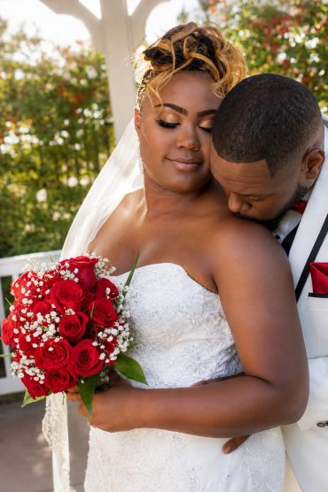 Bride and groom sharing an intimate moment with a bouquet of red roses.