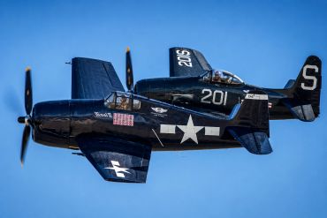 Two vintage navy aircraft flying close together.