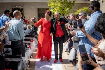 A joyful couple dressed in red and black walking down an aisle at a celebration.