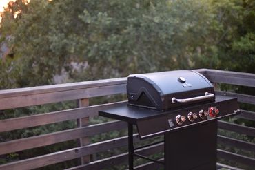 A black outdoor gas grill on a wooden deck surrounded by trees.
